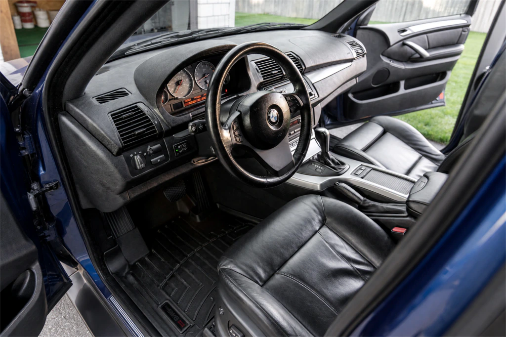 BMW E53 X5 4.8is front cabin showing its analog gauges, steering-wheel controls, center console and leather seat